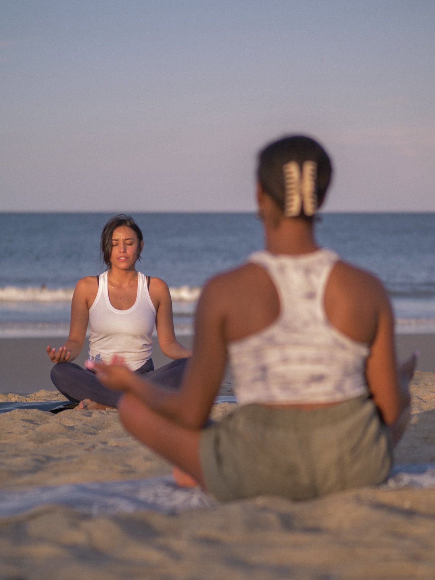 Two people seated in meditation on the beach at sunset