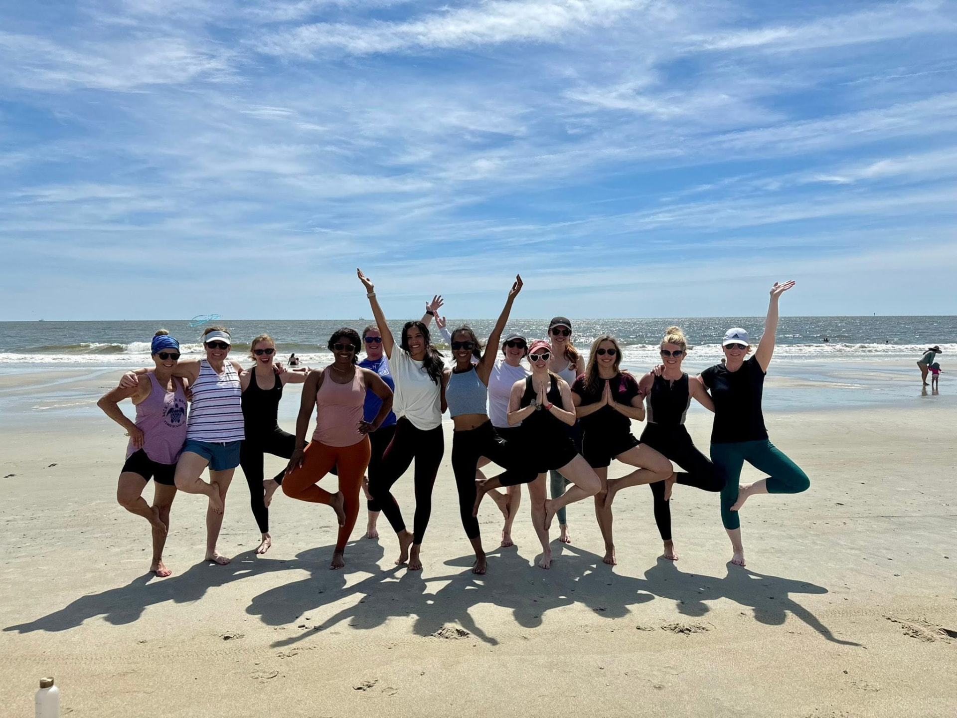 A large community group standing in tree pose together on the beach